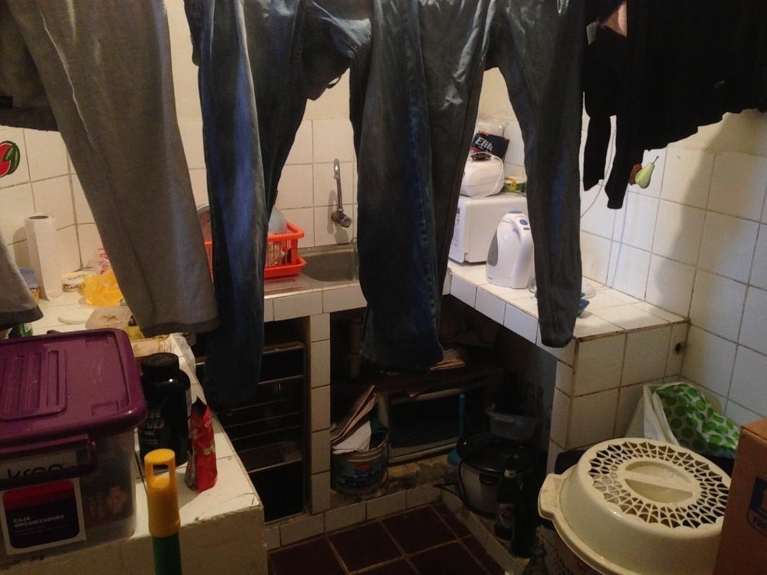Before: a small tiled kitchen with laundry hanging over the sink and cluttered open shelves