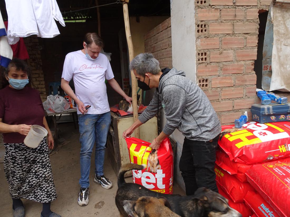 Chris with nail clippers beside a cat while a volunteer opens a food sack