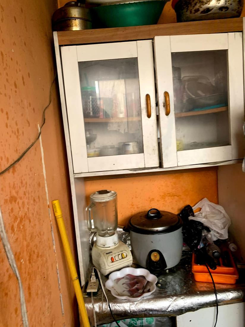 Glass-fronted cupboards above a counter covered in foil, with damp spots on the wall