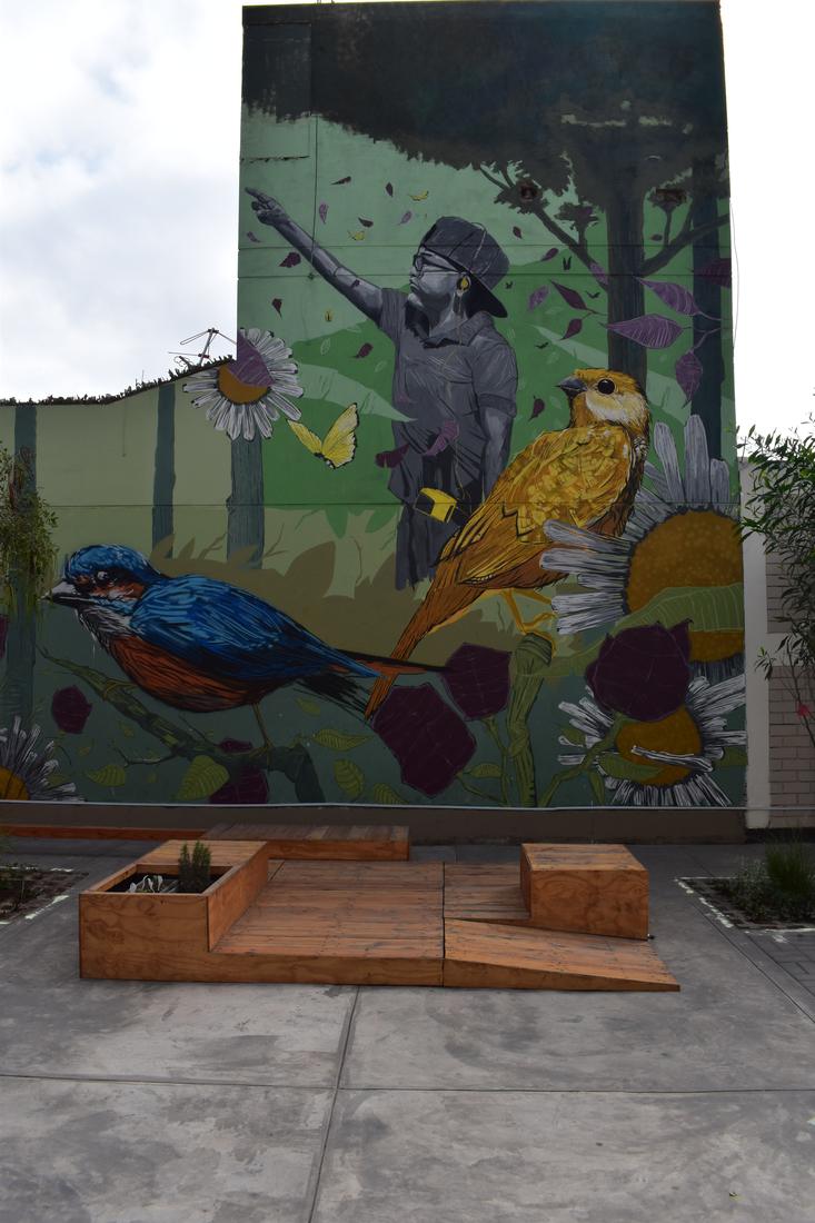 Mural of a boy pointing skyward beside a blue bird and a golden bird, above wooden platforms